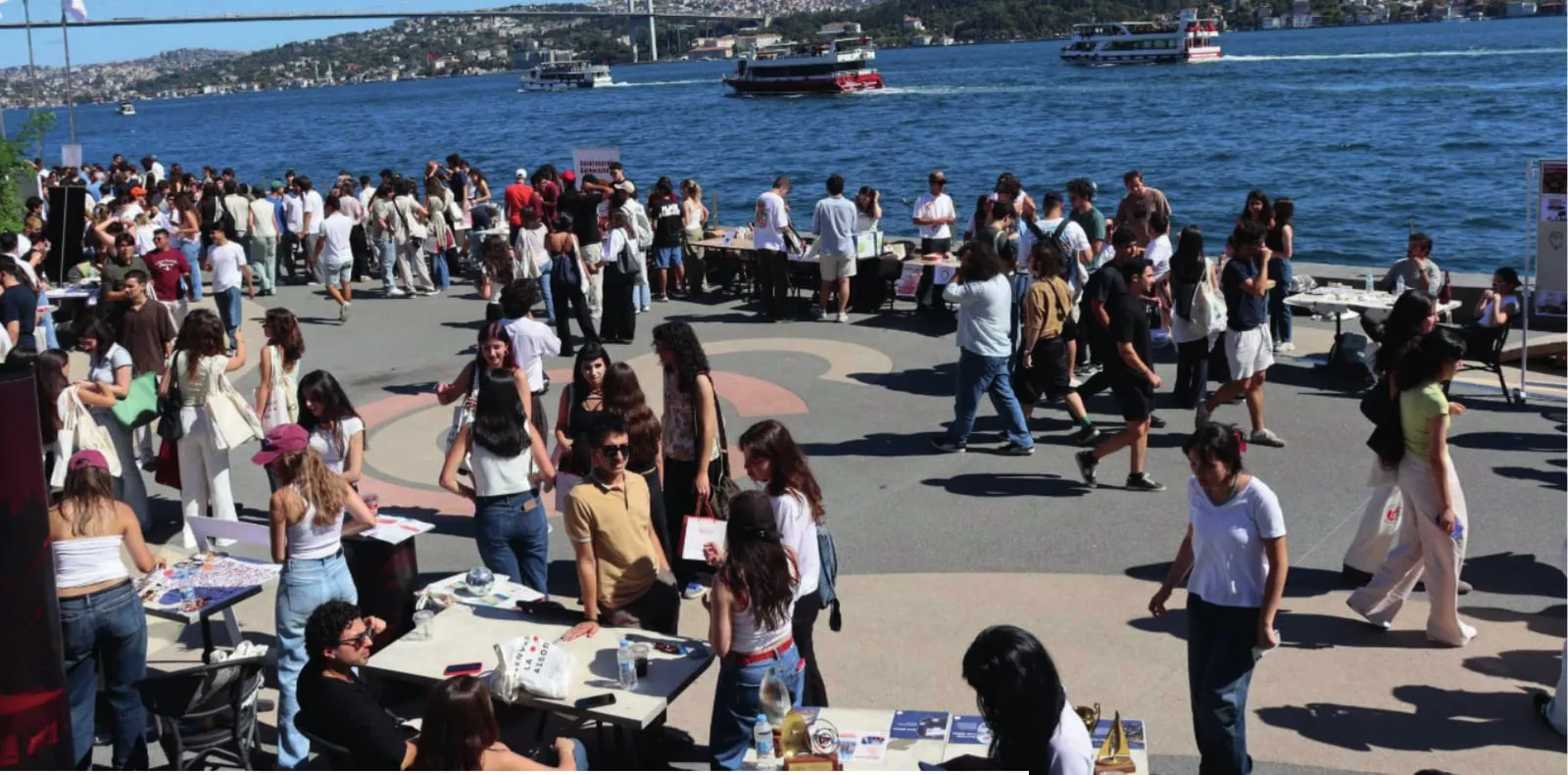 Boğaz kıyısındaki meydanda kulüp masalarının çevresinde toplanmış öğrenciler.